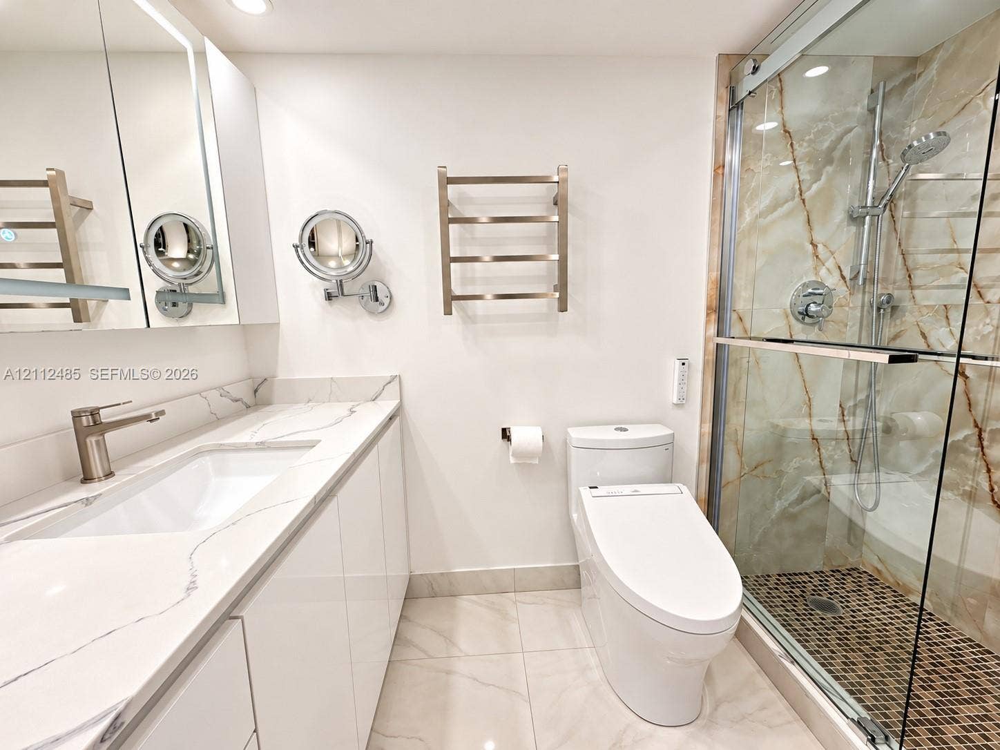 250 174th Street, #1707, Sunny Isles Beach, Sunny Isles Beach, FL 33160 Bathroom featuring a vanity with a white countertop, walk-in shower with glass enclosure and stone-patterned wall tile, wall-mounted heated towel rack, and polished nickel hardware