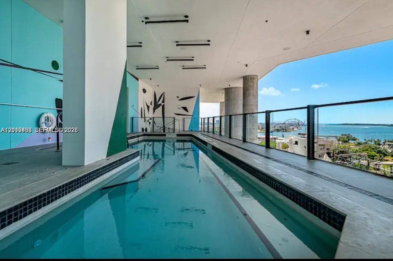 Covered lap pool featuring dark mosaic tile accents, a multi-colored mural wall, recessed ceiling lighting, and a glass panel railing