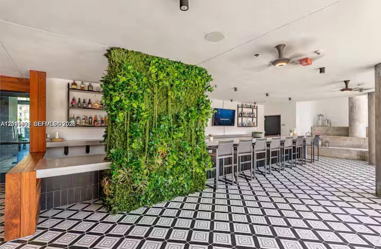 Covered outdoor bar area featuring a geometric-pattern tile floor, a vertical greenery wall, built-in counter seating, and wood-accented structural pillars