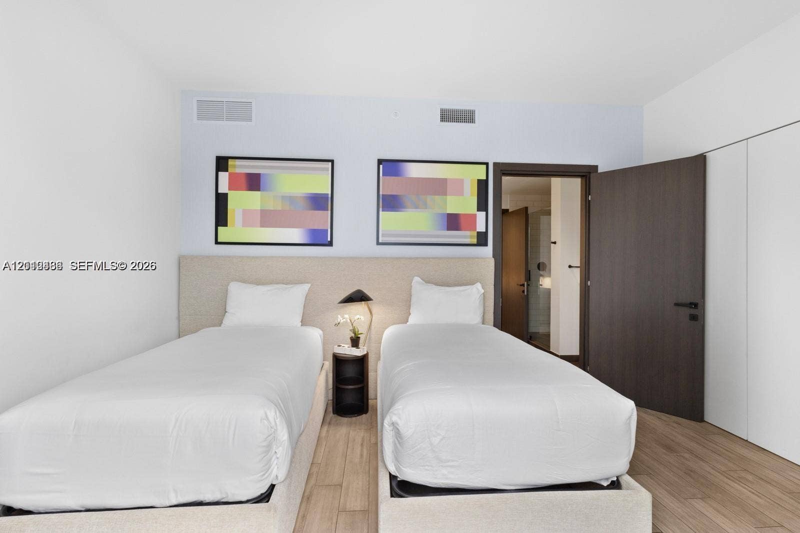Neutral-toned upholstered headboard with integrated nightstand, wood-finish flooring, and dark-finished solid core swing door