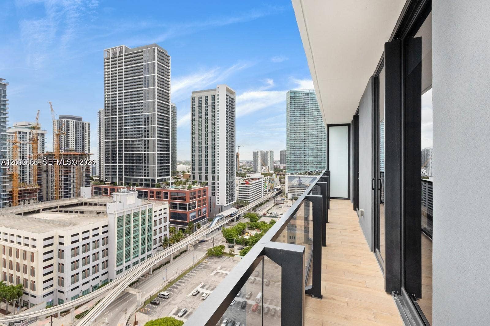 Covered balcony featuring wood-finish flooring, glass panel railings, and metal structural framing