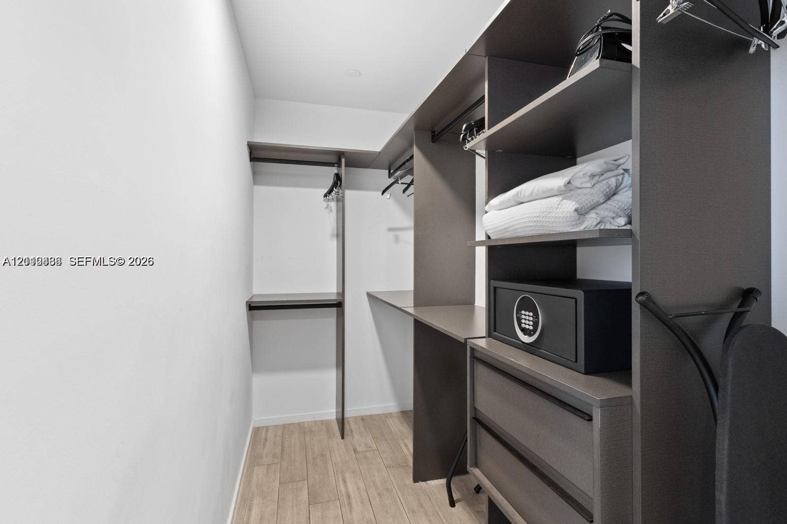 Custom closet system featuring dark wood-finish cabinetry, integrated shelving, hanging rods, and two soft-close drawers, complemented by wood-finish flooring