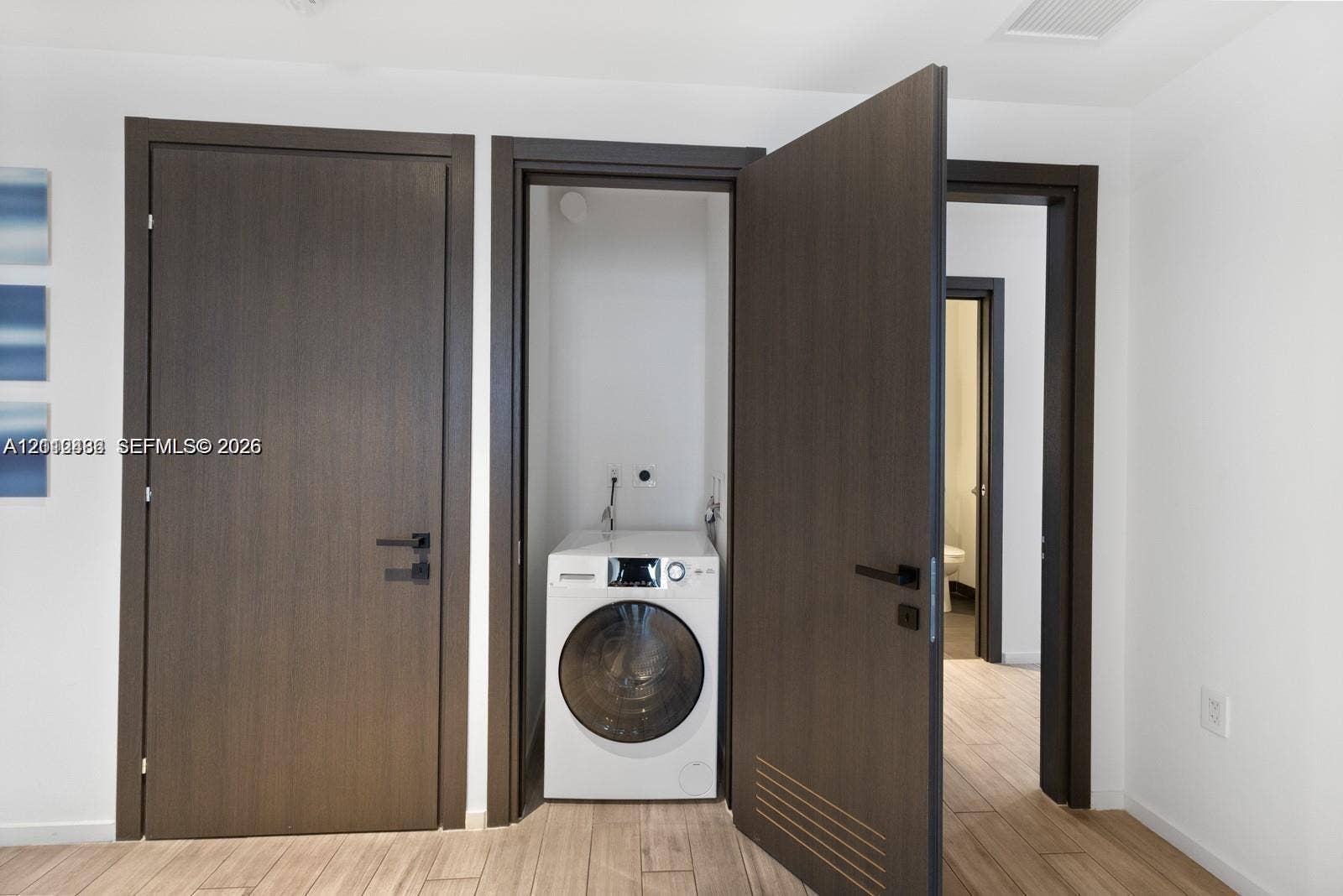 Laundry closet featuring a built-in front-load washer, dark wood-finish interior doors with matte black hardware, and wood-finish flooring