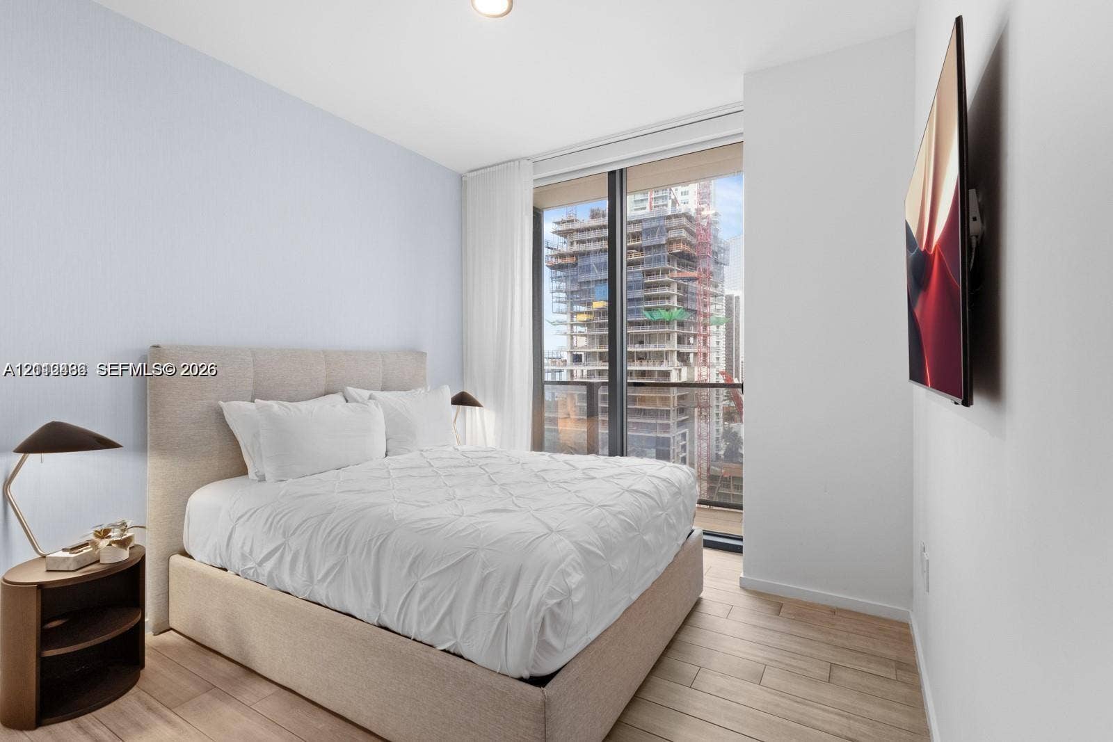 Floor-to-ceiling windows with access to a balcony, wood-finish flooring, and wall-mounted television hardware