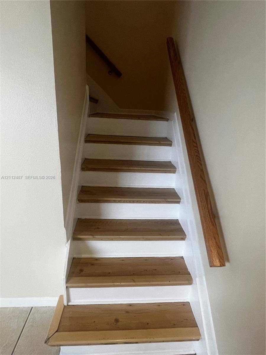 Staircase featuring wood-finish treads, white risers, and a mounted wooden handrail