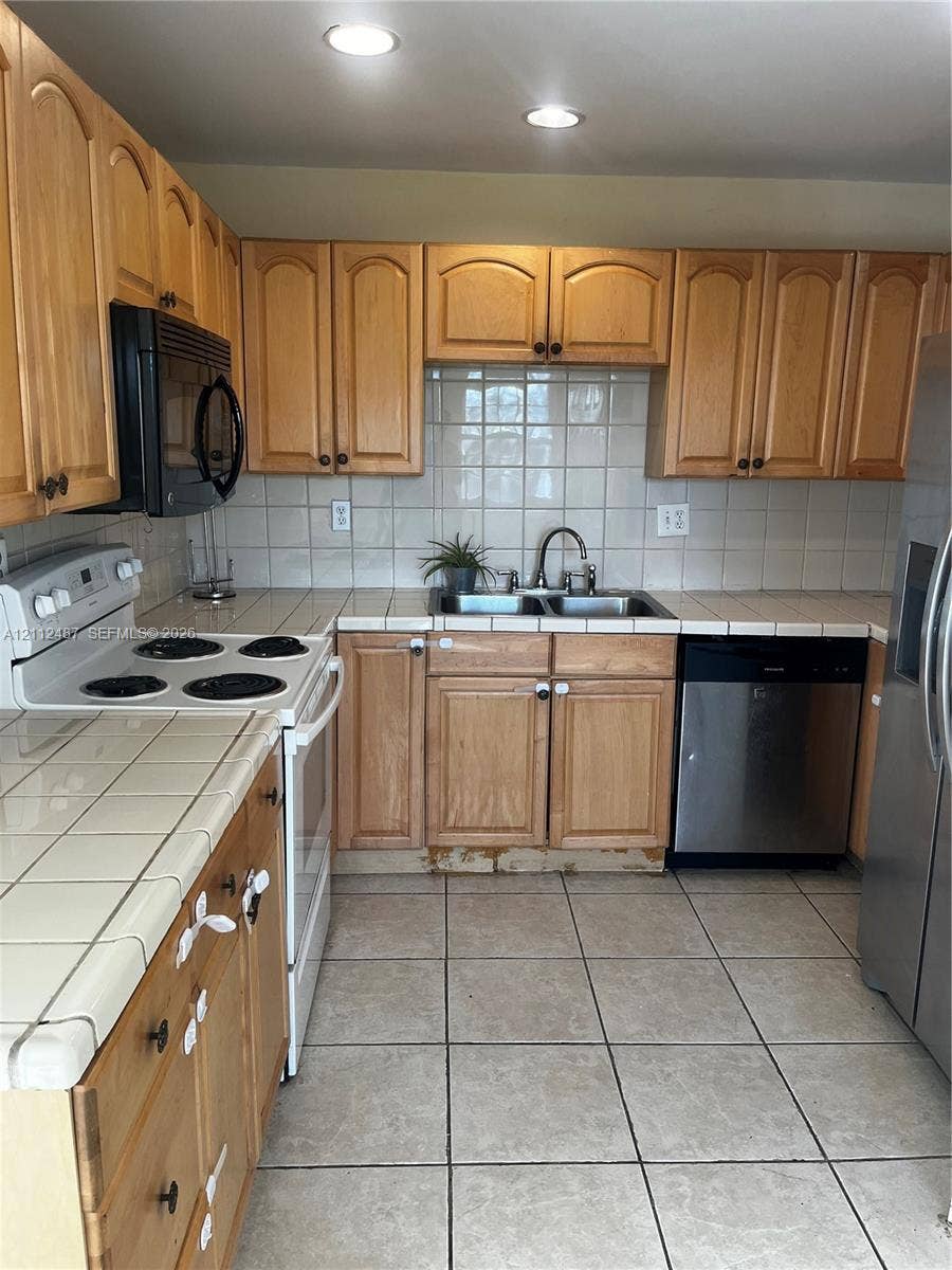 Kitchen featuring wood cabinetry, tiled countertops, tile backsplash, square tile flooring, and stainless steel appliances
