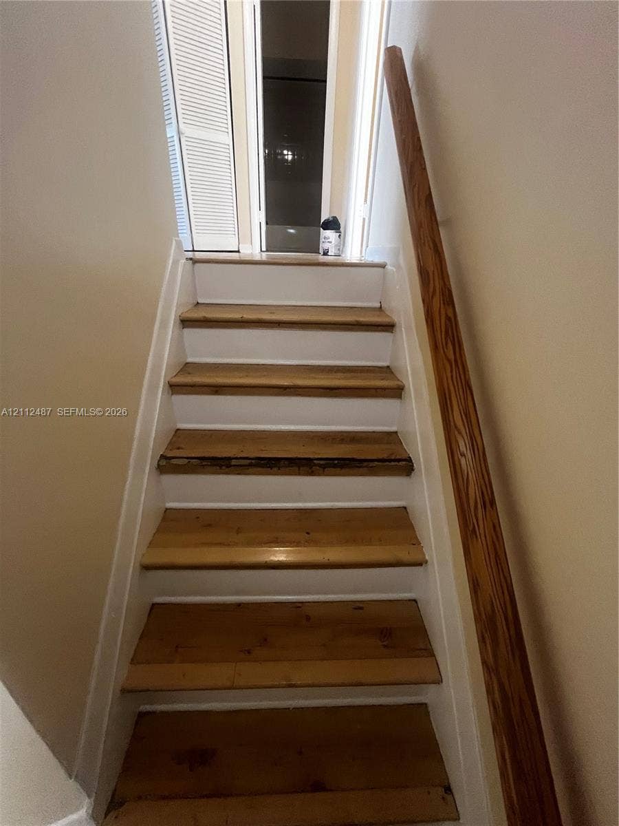 Staircase featuring natural wood treads, white risers, and a mounted wood handrail