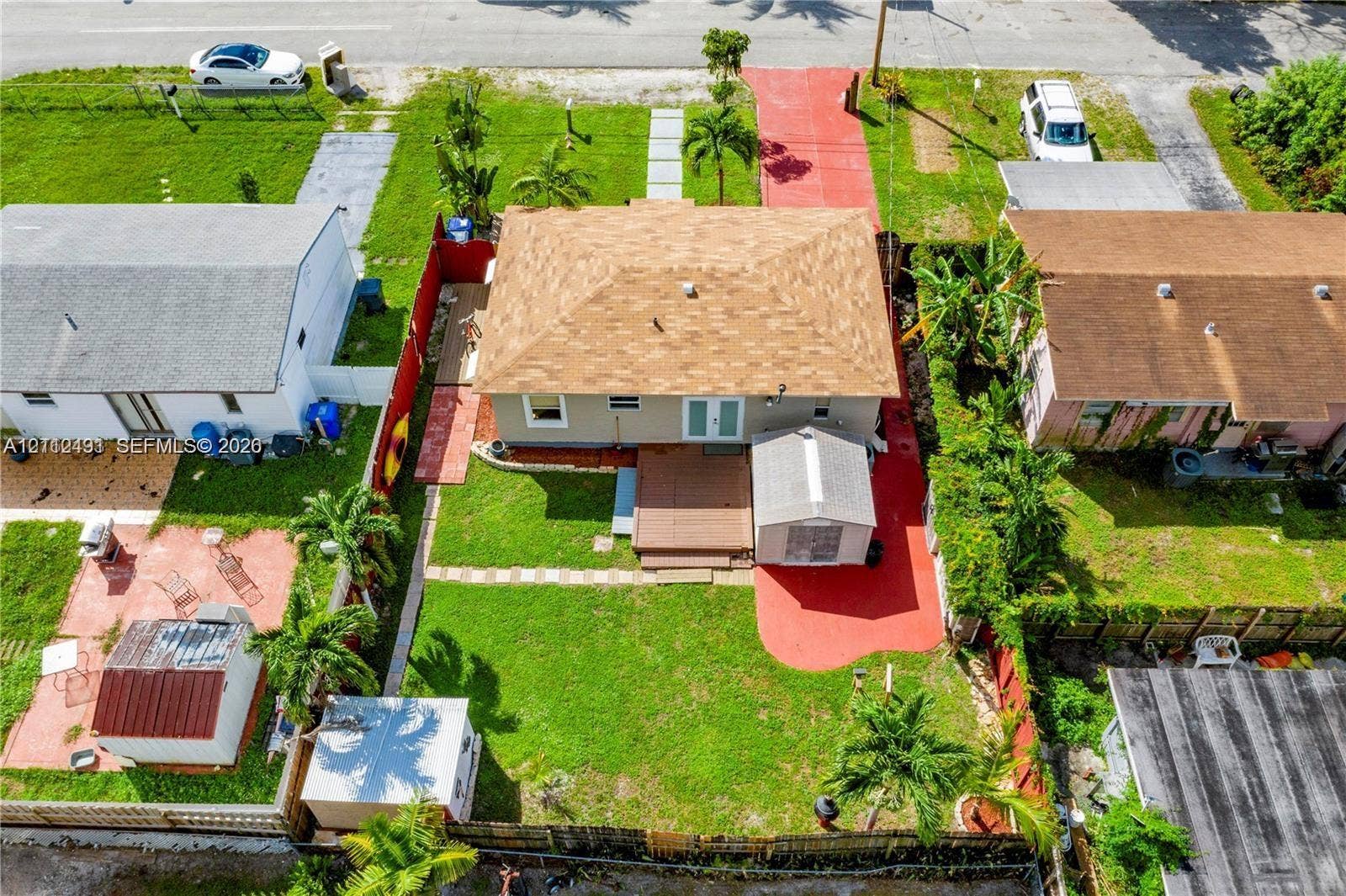 2509 Grant Street, Hollywood, FL 33020 Aerial perspective of a property featuring a hip roof, exterior deck, paved driveway, enclosed backyard, and mature palm trees