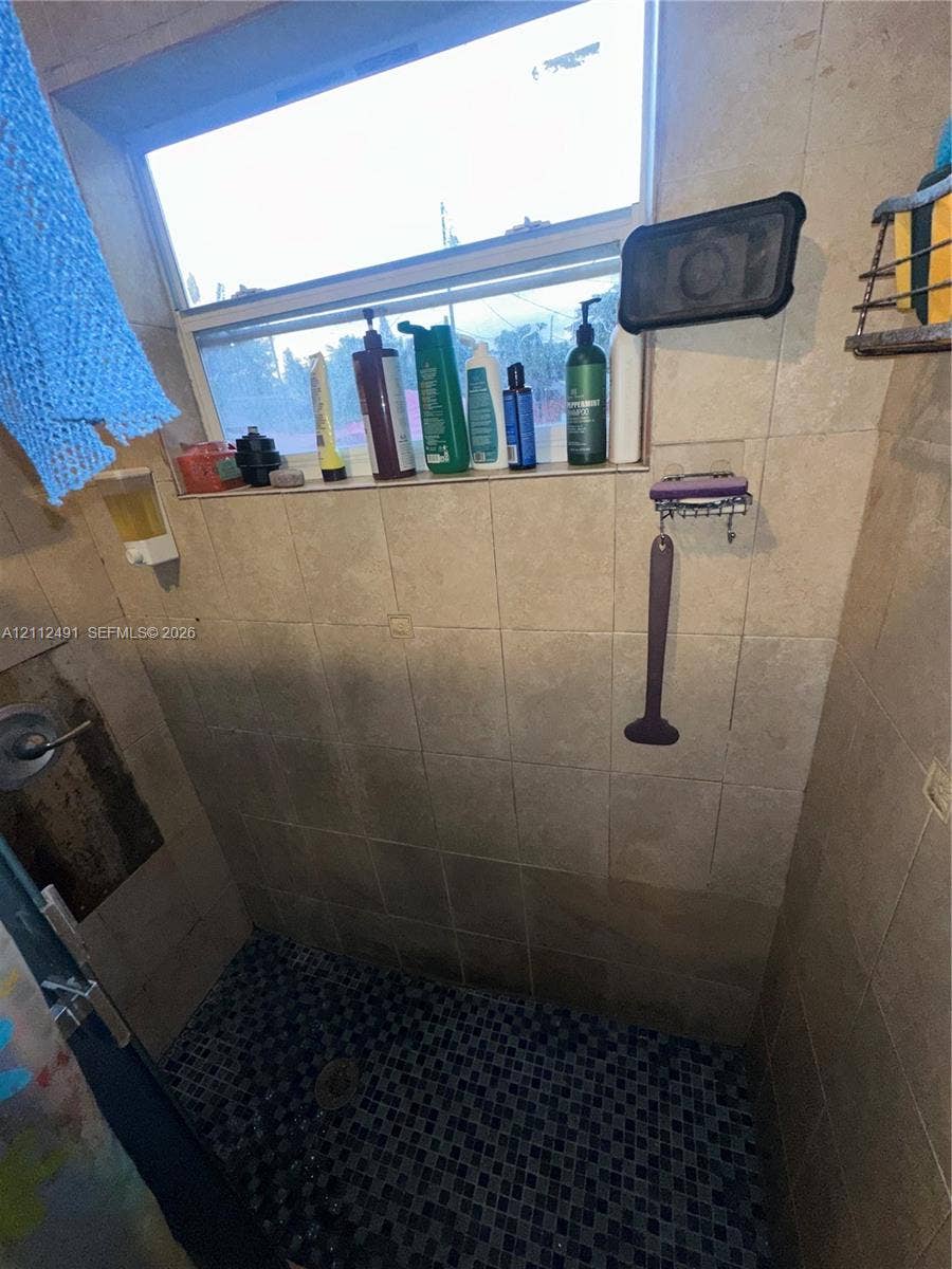 2509 Grant Street, Hollywood, FL 33020 Shower enclosure featuring large-format neutral-toned wall tiles, dark mosaic floor tiling, and an integrated horizontal tile shelf