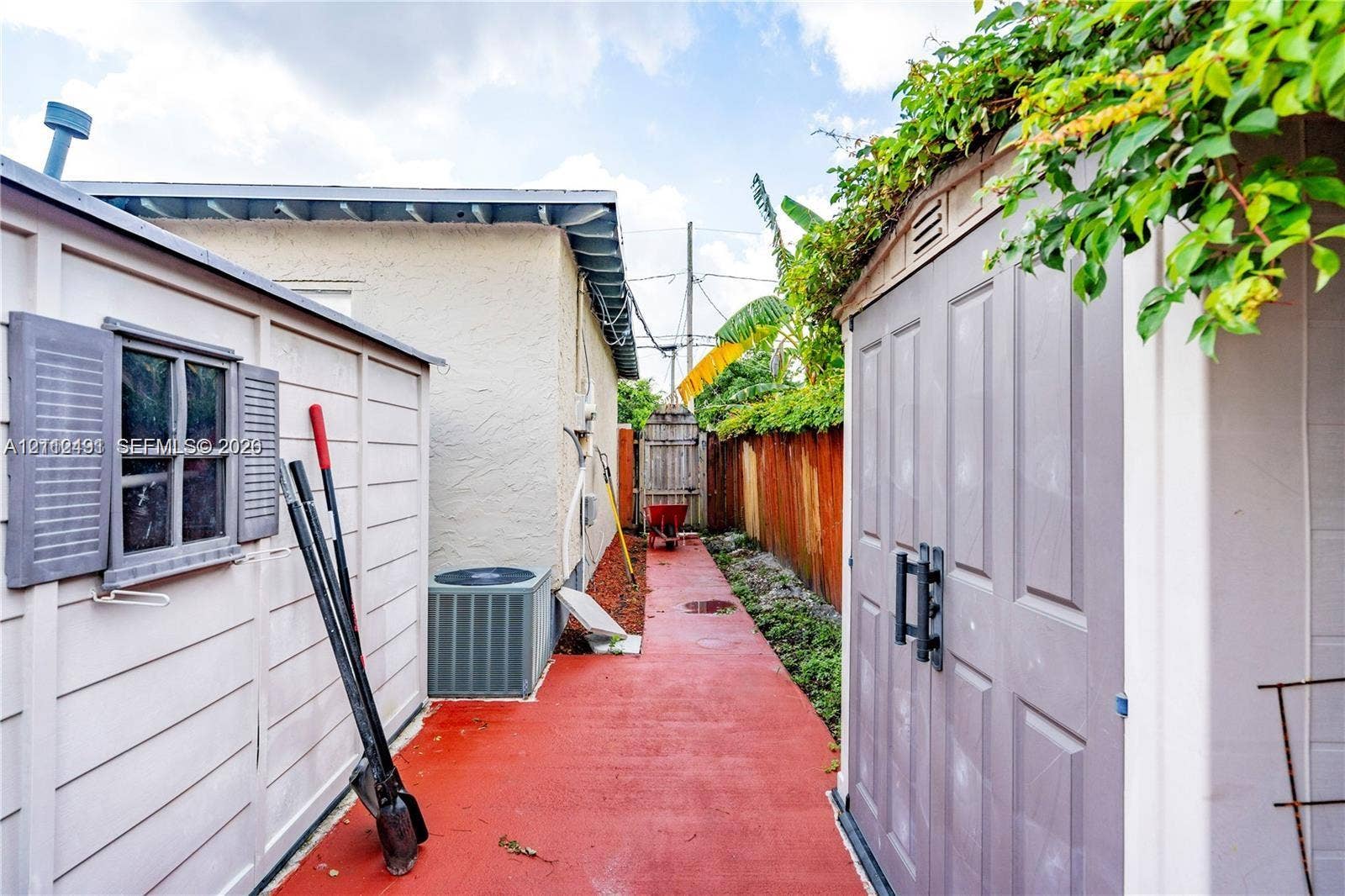 2509 Grant Street, Hollywood, FL 33020 Side exterior area featuring a paved walkway, two storage structures, and perimeter wood fencing