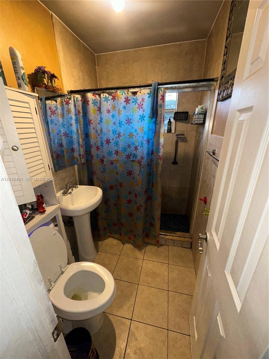 2509 Grant Street, Hollywood, FL 33020 Bathroom featuring large-format tile flooring, pedestal sink, and tiled shower surround with a metal rod fixture