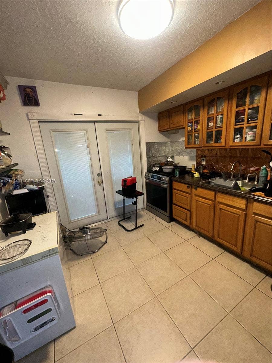 2509 Grant Street, Hollywood, FL 33020 Kitchen featuring wood cabinetry with glass-panel upper doors, tile flooring, stainless steel range, and double glass-paneled exterior doors