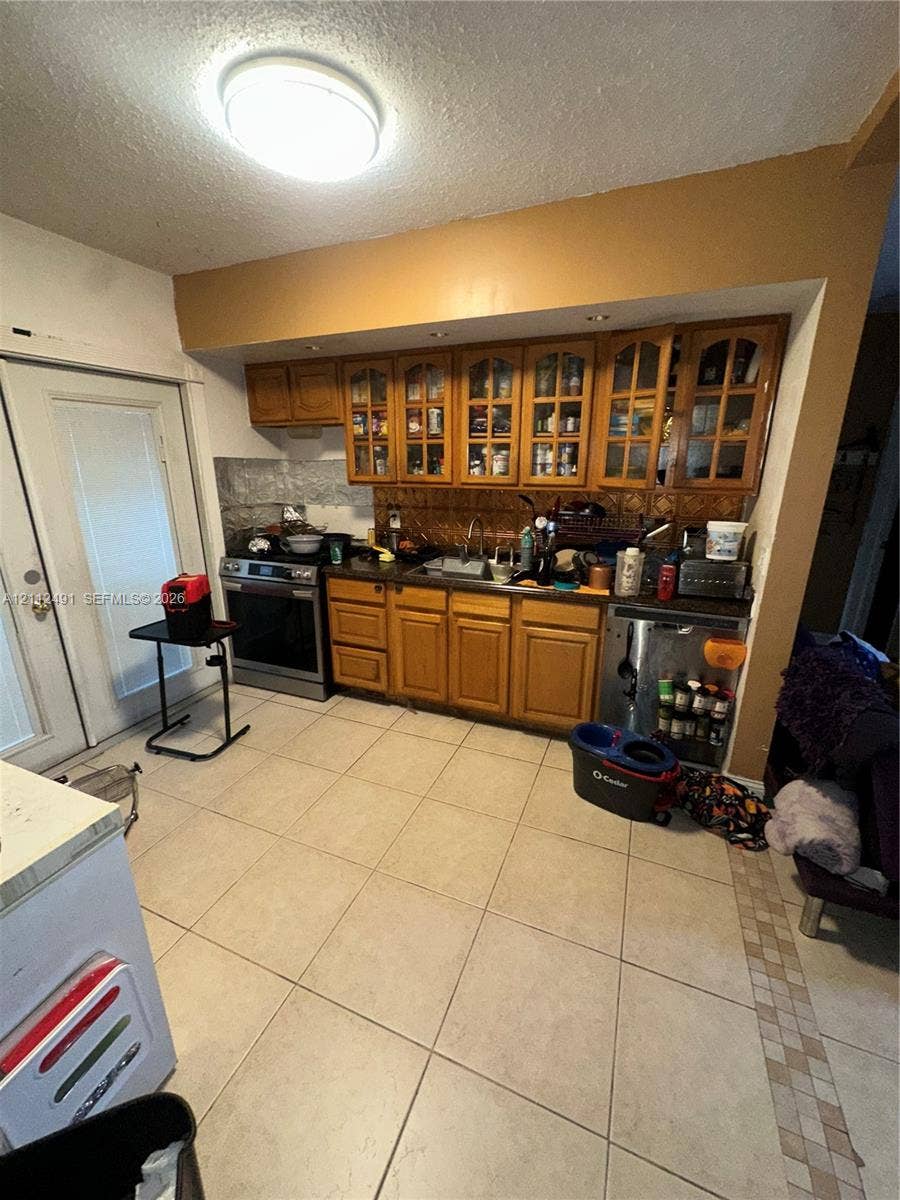 2509 Grant Street, Hollywood, FL 33020 Kitchen featuring light wood cabinetry with glass-panel upper doors, stainless steel oven, stone-finish backsplash, and large-format ceramic tile flooring