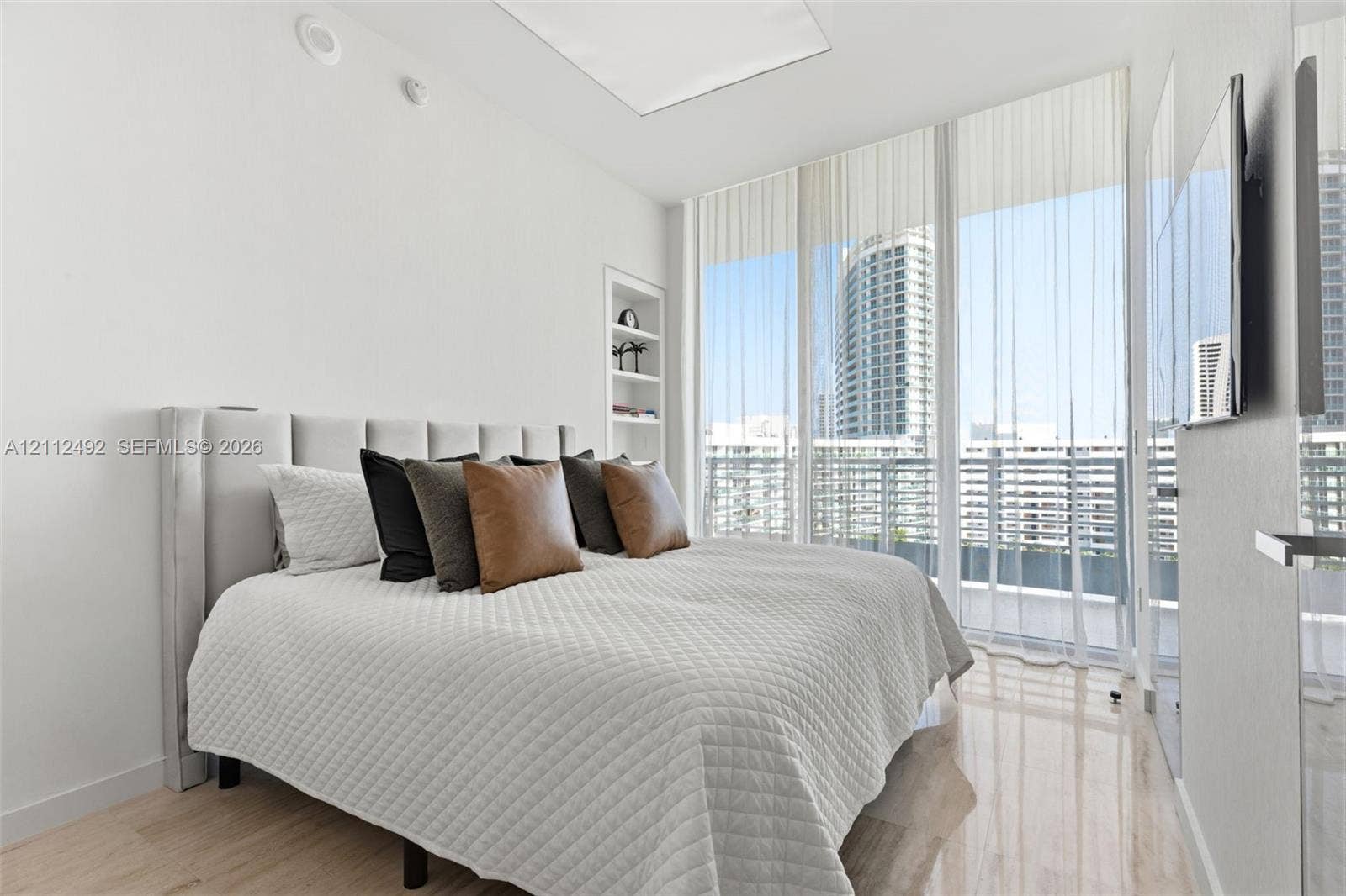 Floor-to-ceiling windows, light-toned wood-finish flooring, built-in shelving, and high-contrast urban scenery