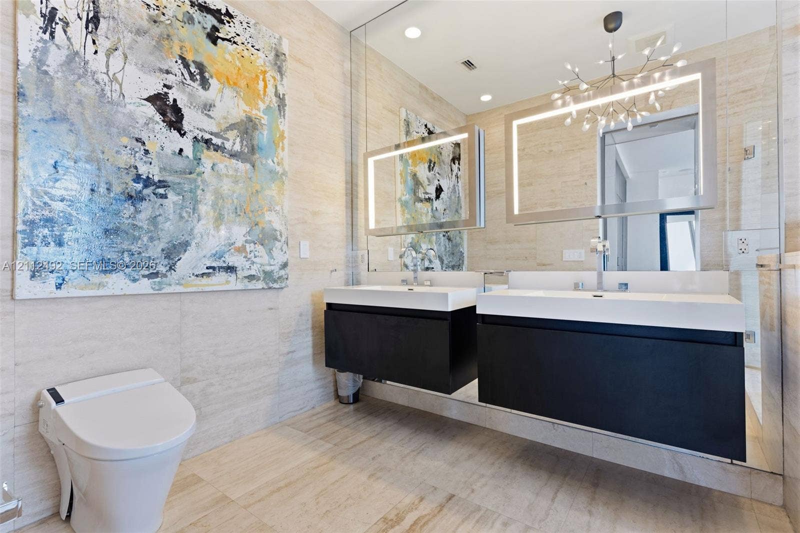 Floating dual vanity with integrated white basins, illuminated rectangular mirrors, full-wall stone-tile surfacing, and a sleek low-profile toilet