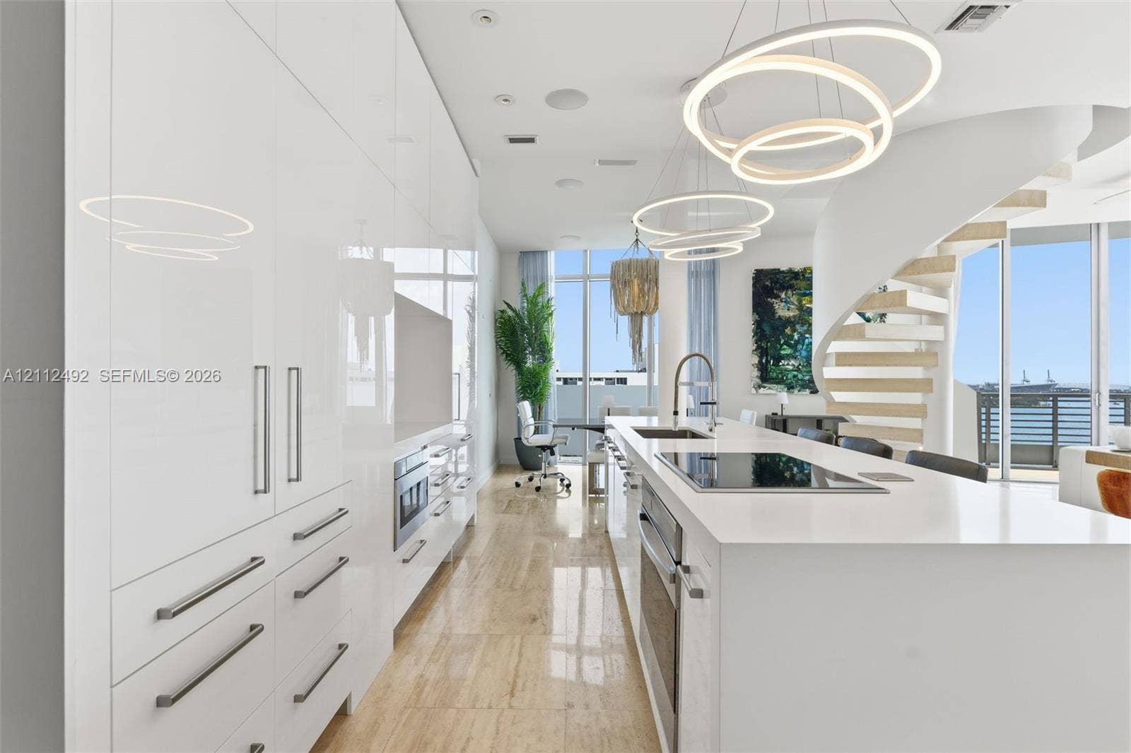 High-gloss cabinetry, stone-surfaced kitchen island, integrated stainless steel appliances, circular pendant lighting, and a sculptural spiral staircase with floating treads