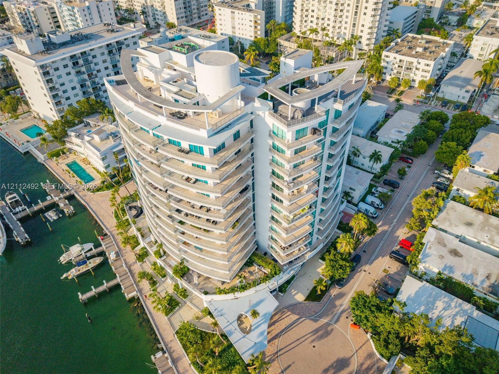High-rise multi-story building featuring curvilinear architectural design, extensive glass-paneled balconies, a rooftop terrace, and a private dock facility on the water