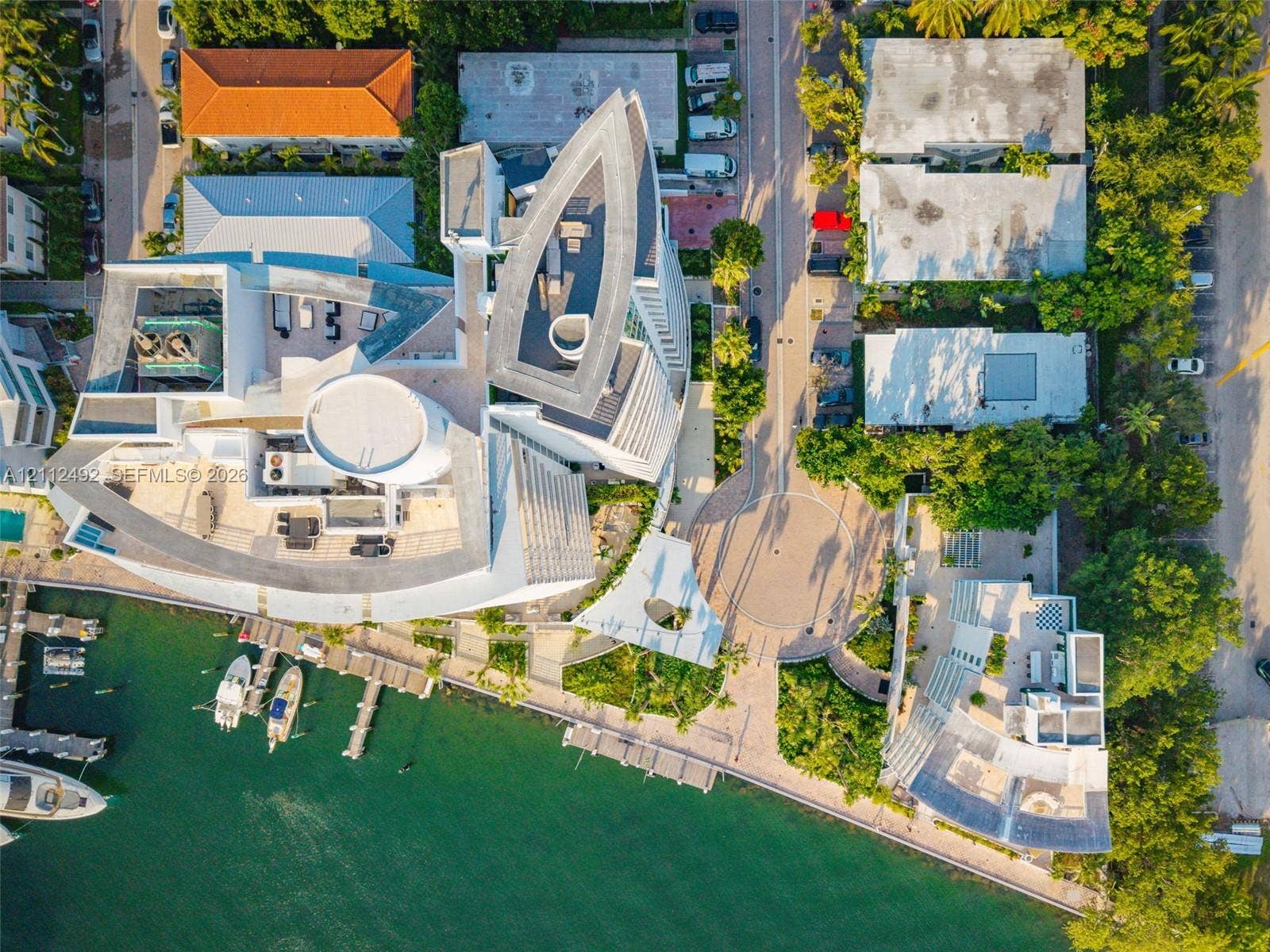 Aerial perspective of a multi-level waterfront estate featuring a private deep-water dock, extensive rooftop terrace space, and hardscaped circular motor court