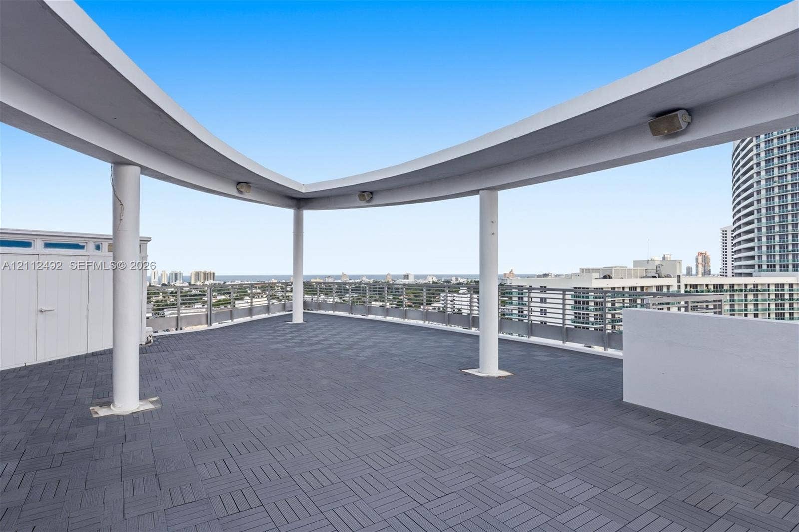 Rooftop terrace featuring dark modular interlocking flooring, a curved architectural canopy supported by cylindrical columns, and metal perimeter railing