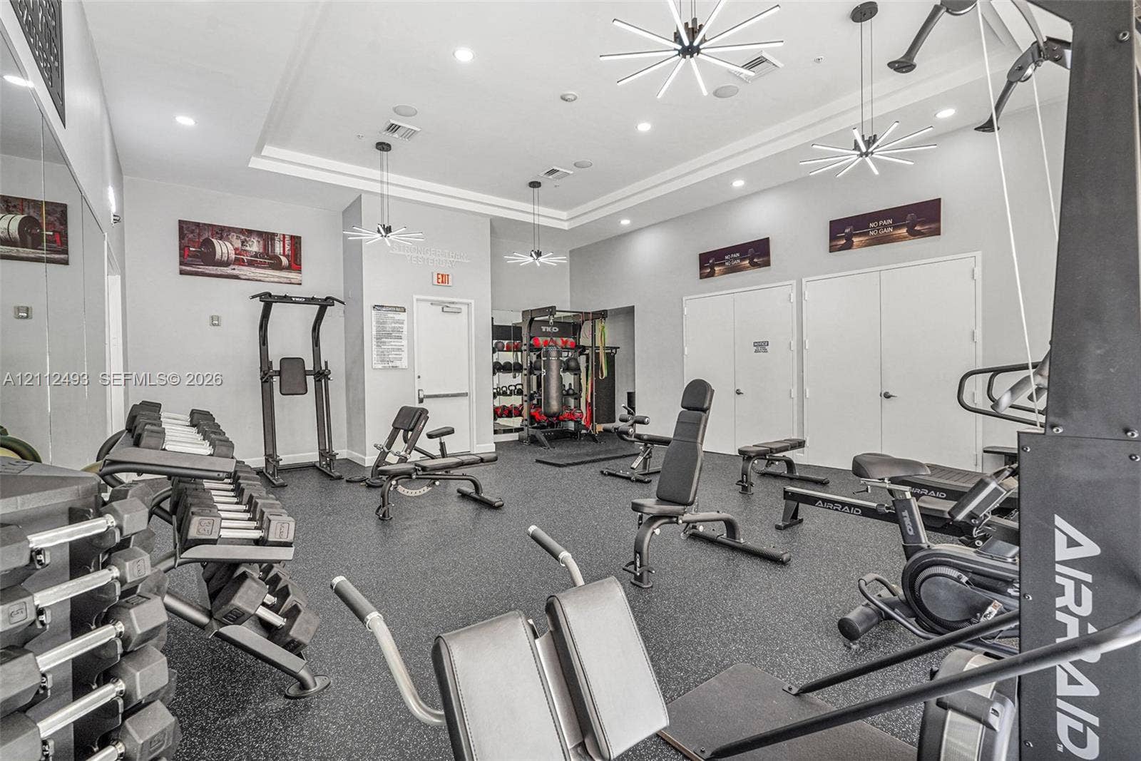 Fitness center featuring rubberized flooring, recessed lighting, modern tiered chandeliers, and wall-to-wall mirrors