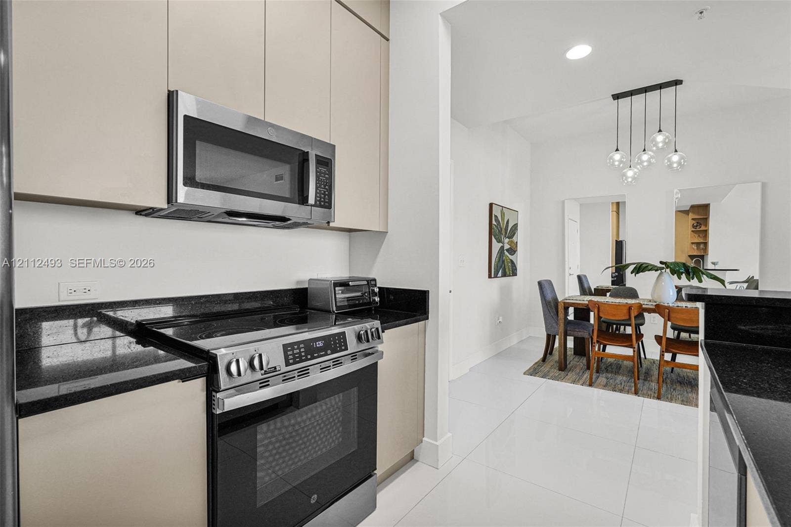 Kitchen featuring light-finish cabinetry, black stone countertops, stainless steel appliances, and large-format tile flooring