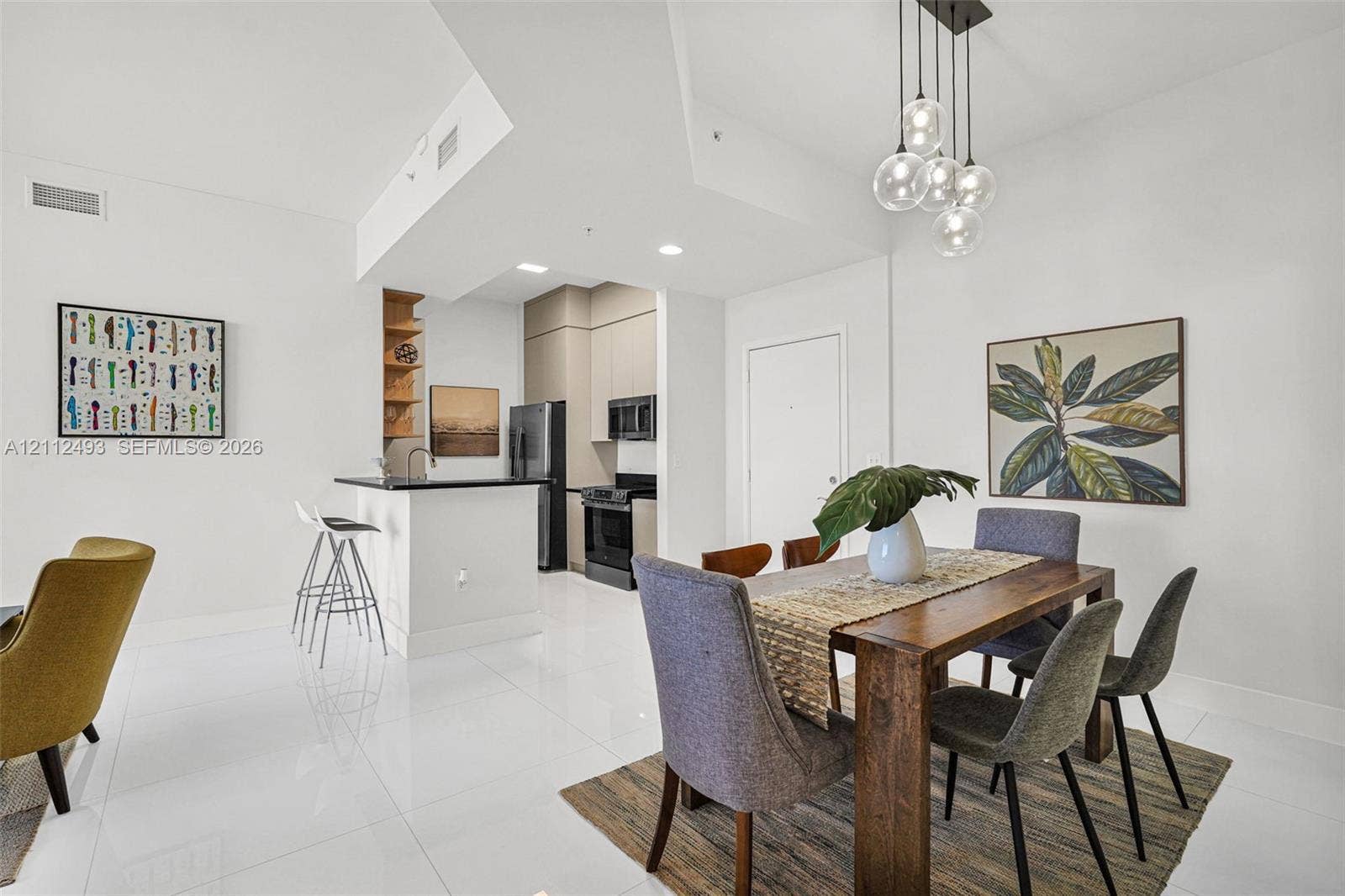 Kitchen featuring full-height cabinetry, stone-surfaced breakfast bar, and stainless steel appliances, illuminated by a multi-bulb glass pendant fixture and polished tile flooring