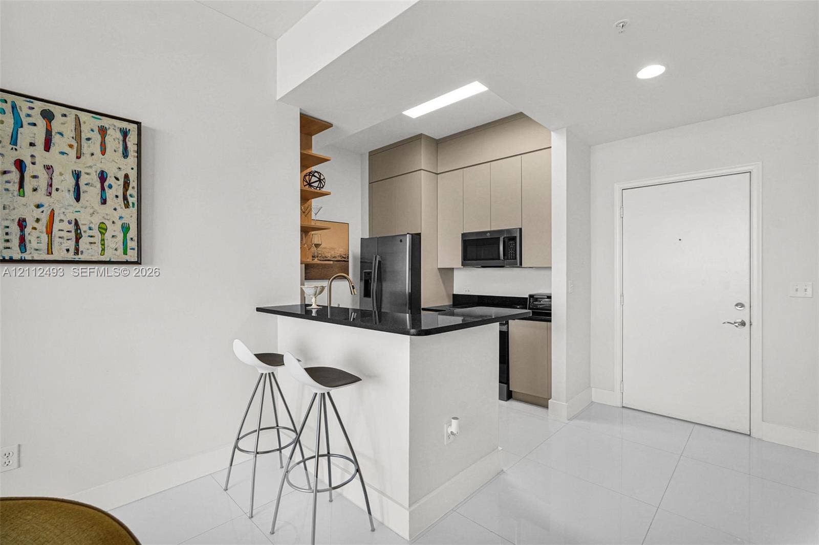 Kitchen featuring a breakfast bar with stone-surfaced countertop, integrated flat-panel cabinetry, built-in microwave, and large-format tile flooring