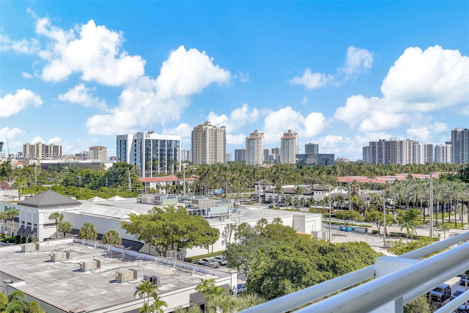 Elevated balcony featuring a white metal railing overlooking a cityscape and mature palm trees