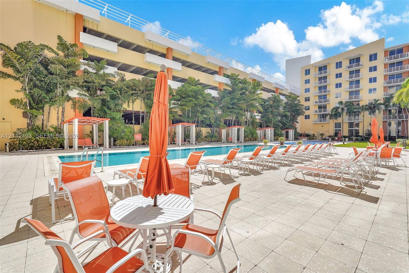 Outdoor swimming pool featuring a paved deck, multiple cabanas, and mature palm trees