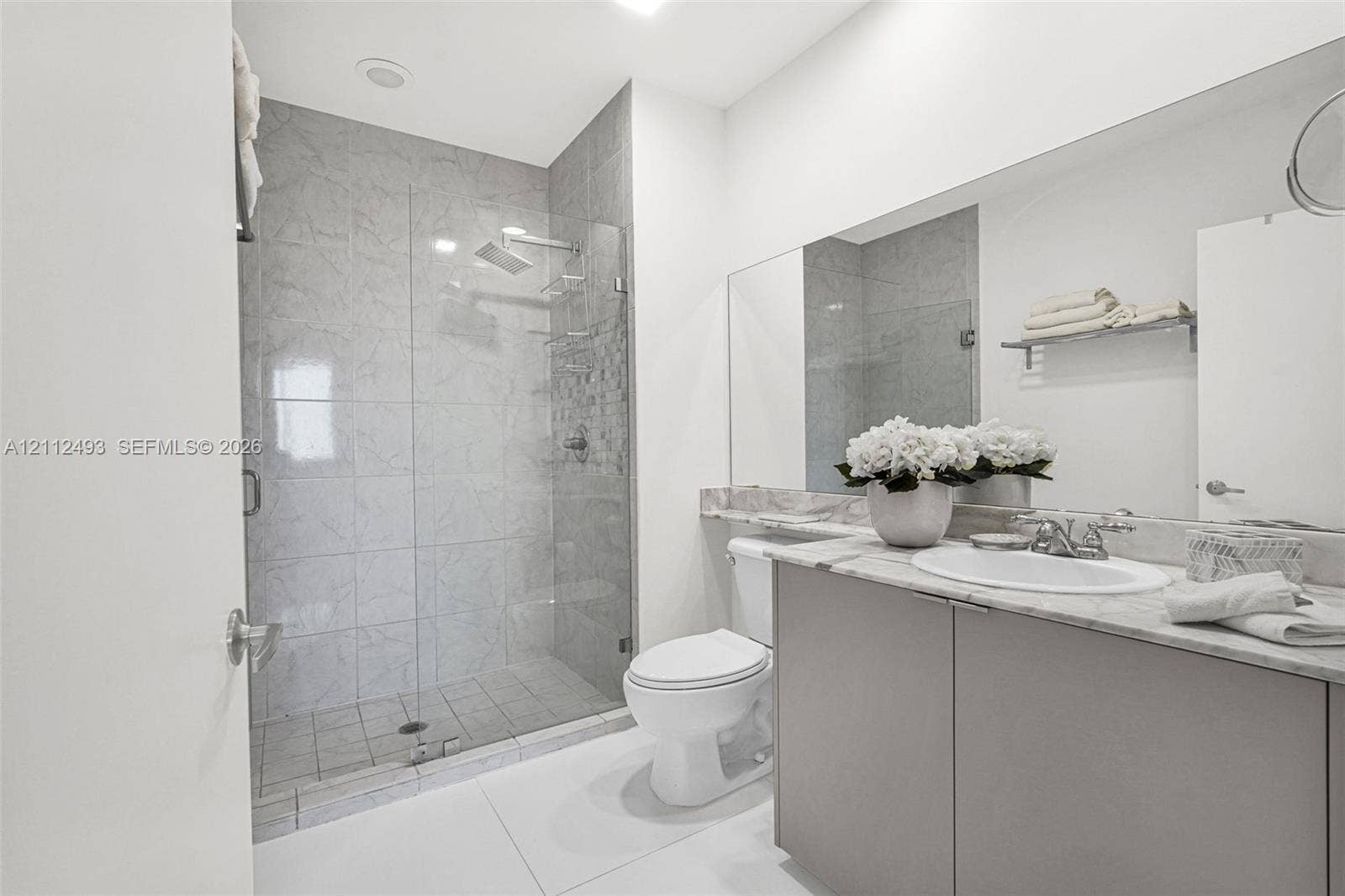 Walk-in shower with floor-to-ceiling tile, frameless glass enclosure, and rain-style showerhead, complemented by a vanity with stone-finish countertop and integrated sink