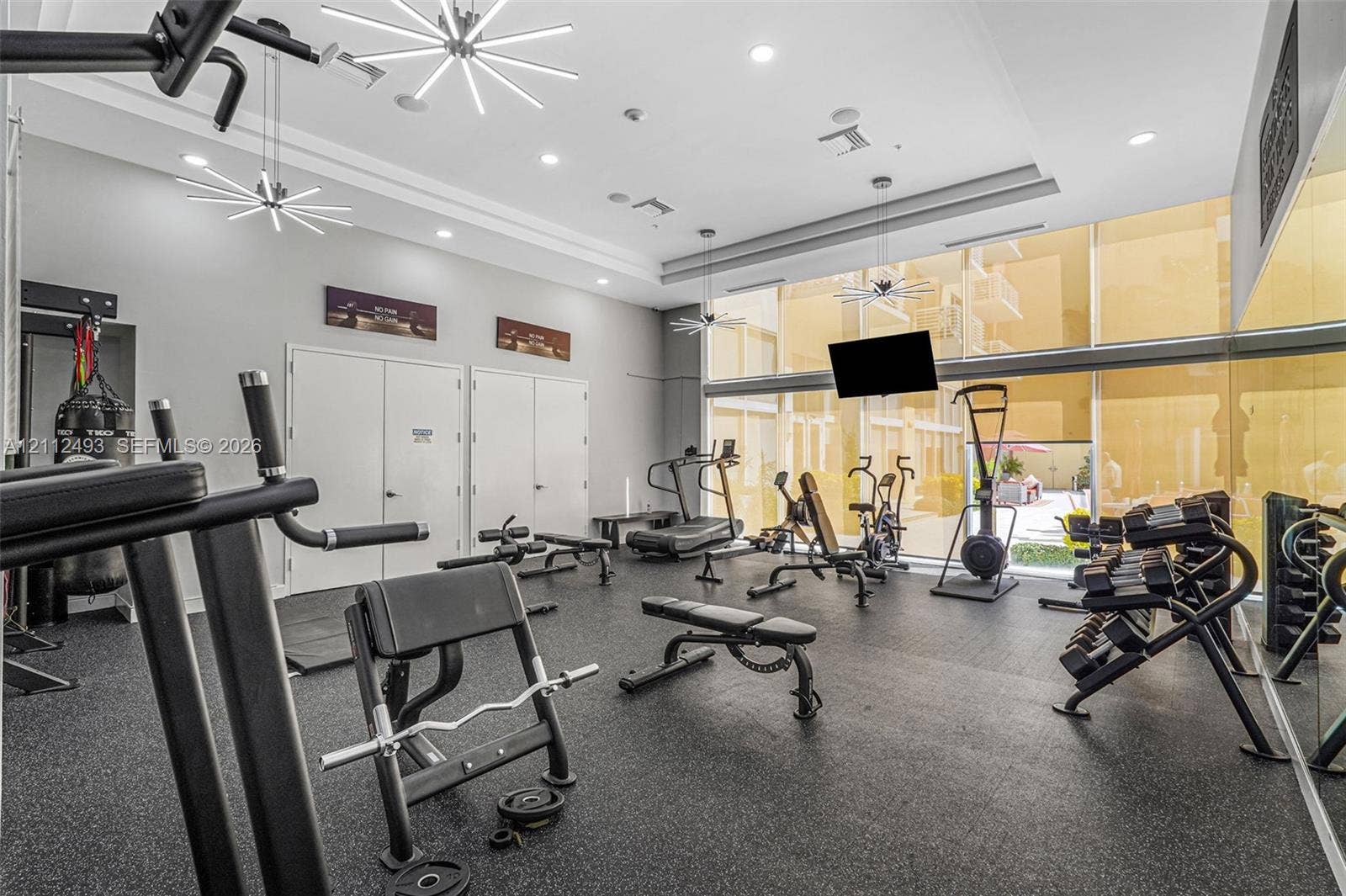 Fitness space featuring floor-to-ceiling windows, high ceilings with multi-arm sputnik-style chandeliers, recessed lighting, and rubberized flooring