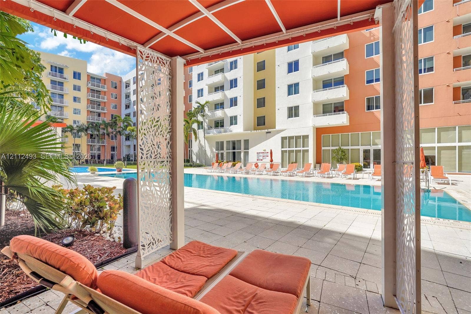 Outdoor covered cabana featuring laser-cut metal privacy panels and a tension-fabric canopy, situated on a stone-paved deck with a rectangular swimming pool