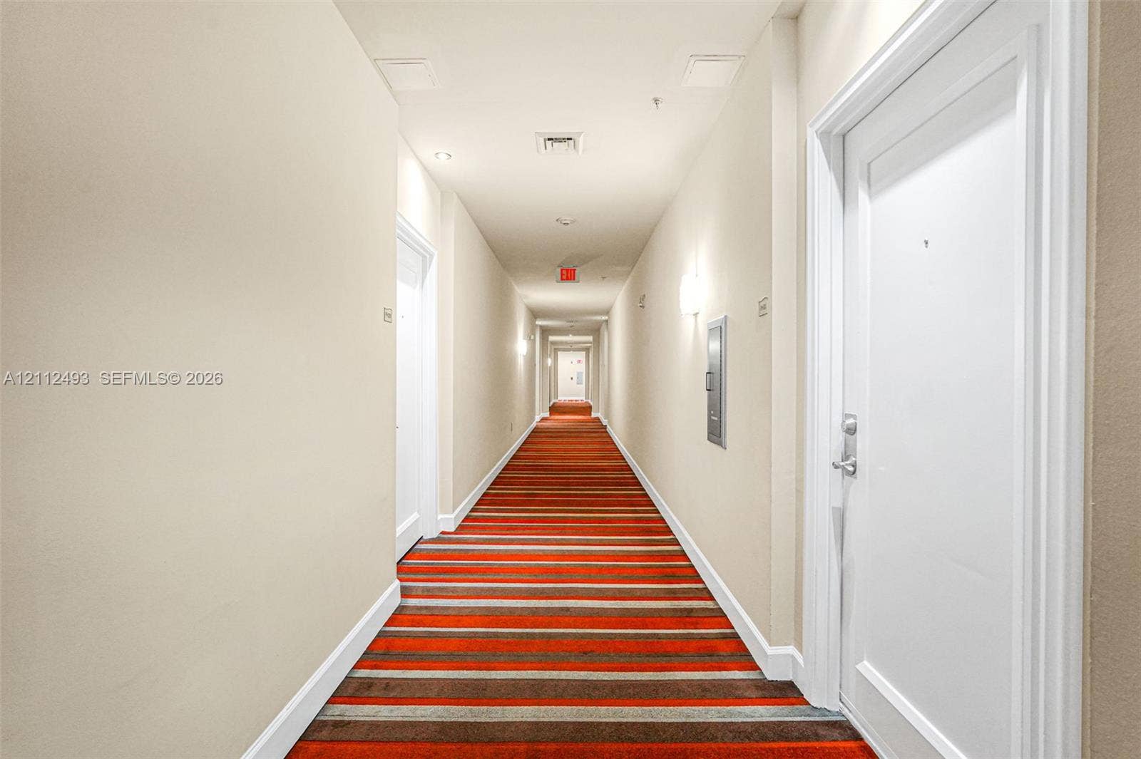 Interior hallway featuring striped carpeting, solid-core doors, and wall-mounted sconce lighting