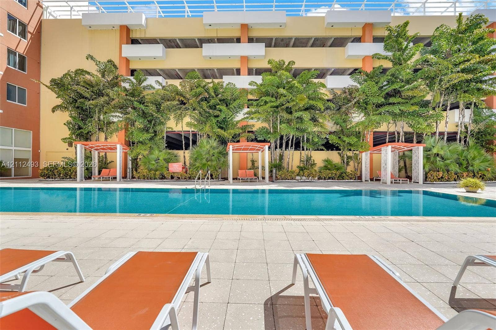 Swimming pool with tiled decking, mature landscaping, and covered cabanas
