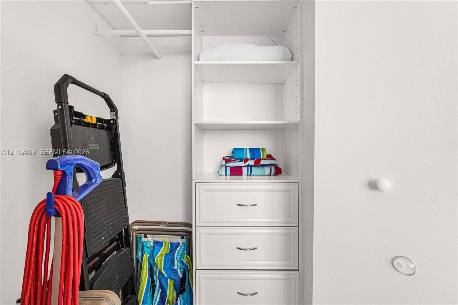 Built-in storage closet featuring white cabinetry, three pull-out drawers with metallic hardware, and adjustable open shelving