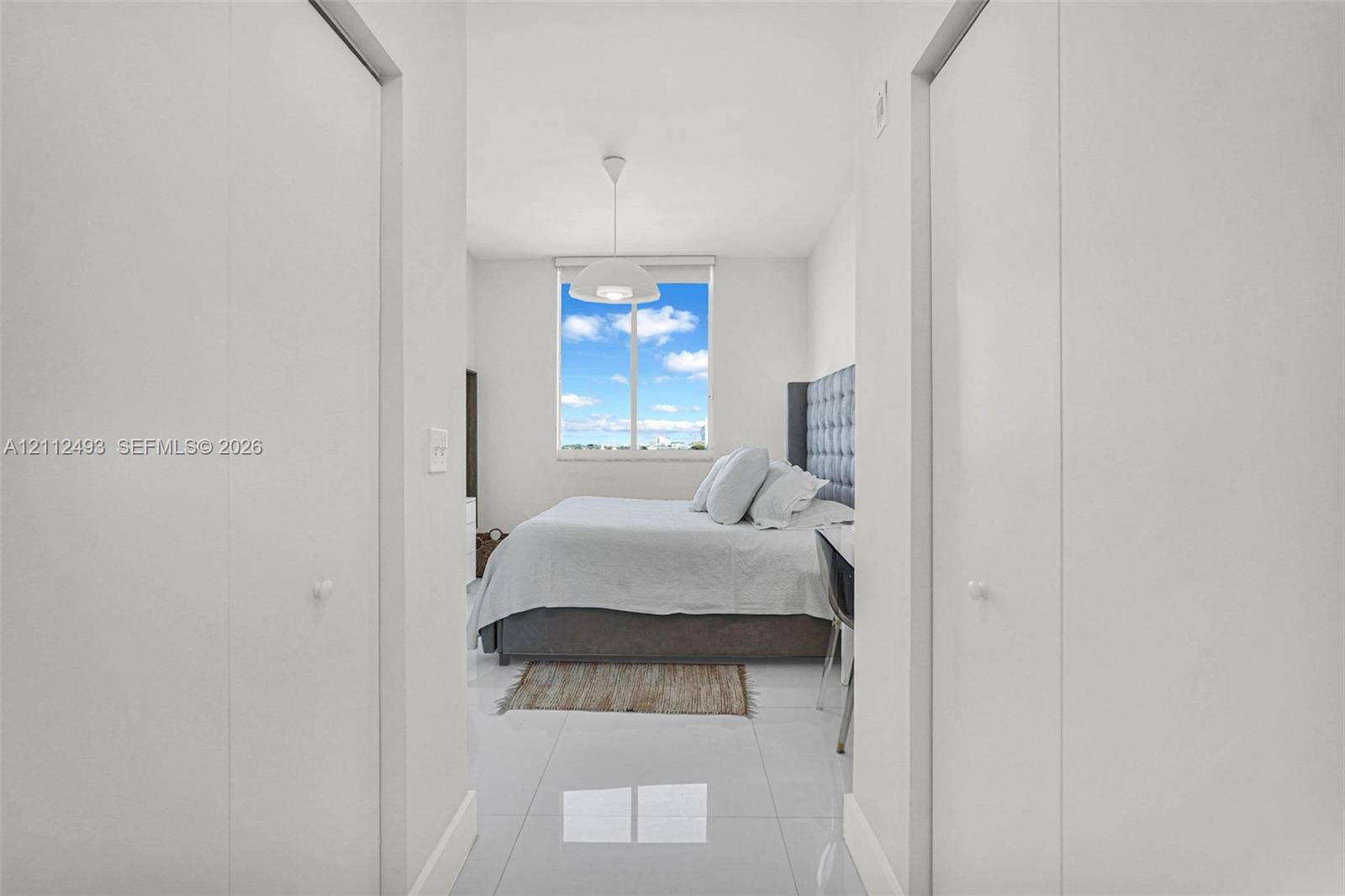 Neutral interior featuring large-format tile flooring, dual floor-to-ceiling closets, and an oversized window providing natural light