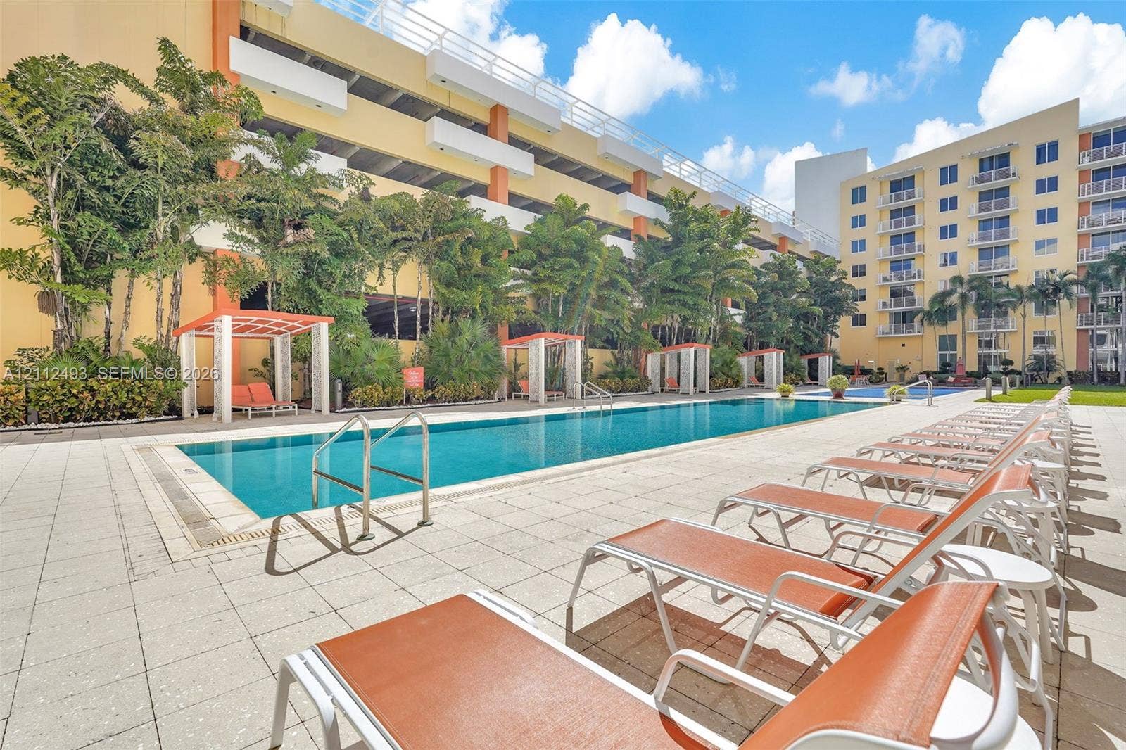 Swimming pool featuring a tiled deck, integrated cabanas, metal handrails, and mature landscaping