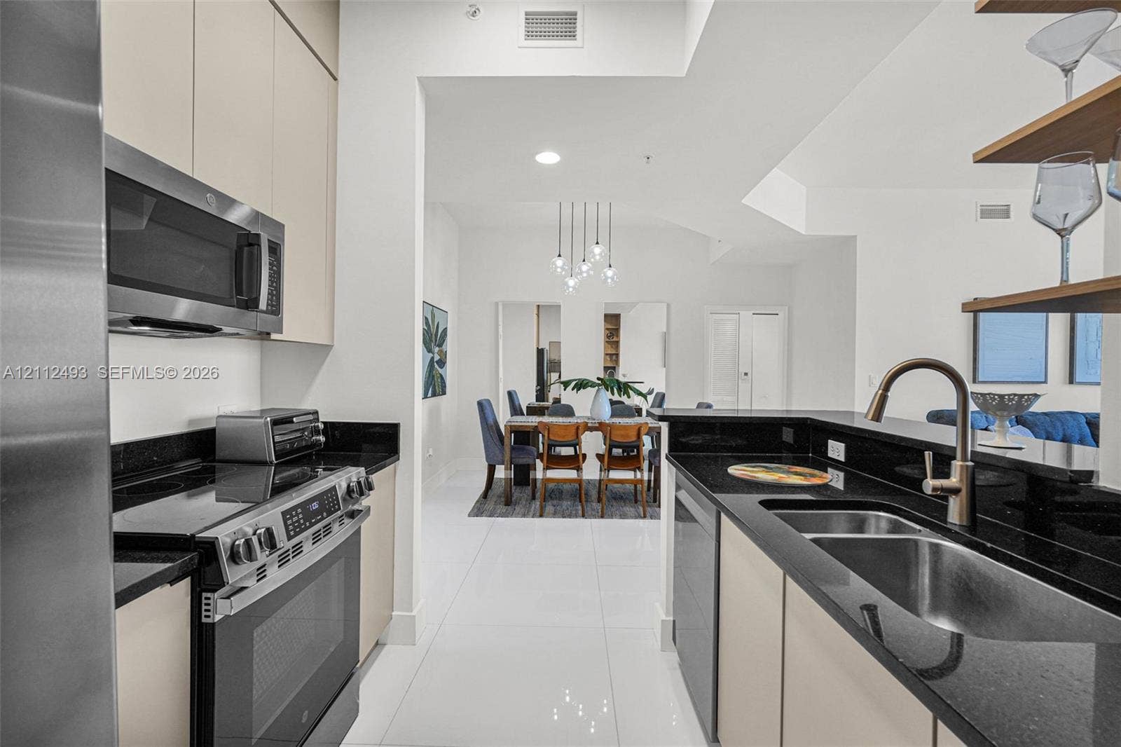 Kitchen featuring flat-panel cabinetry, dark stone countertops, stainless steel appliances, dual-basin stainless steel sink, and polished tile flooring