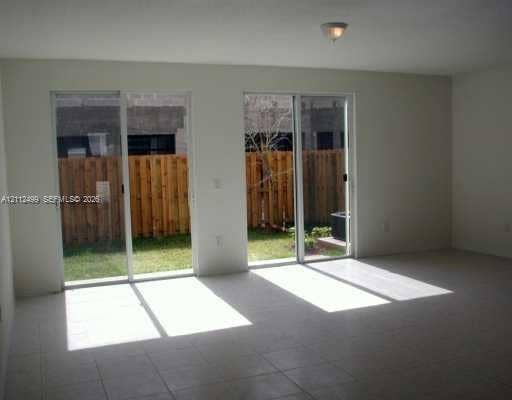 Living area featuring tile flooring, neutral wall tones, and dual sliding glass doors providing outdoor access