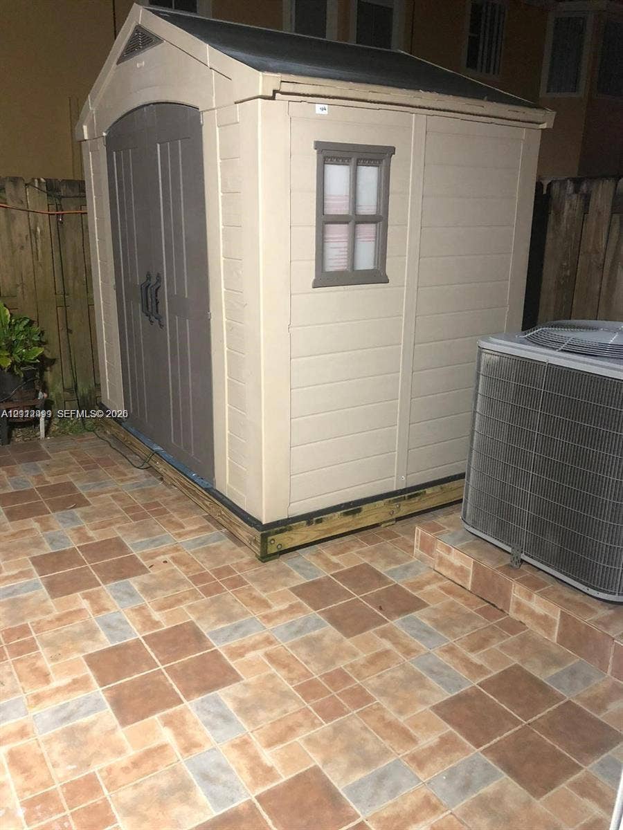 Exterior storage structure with double doors and window, set upon a paved patio surface