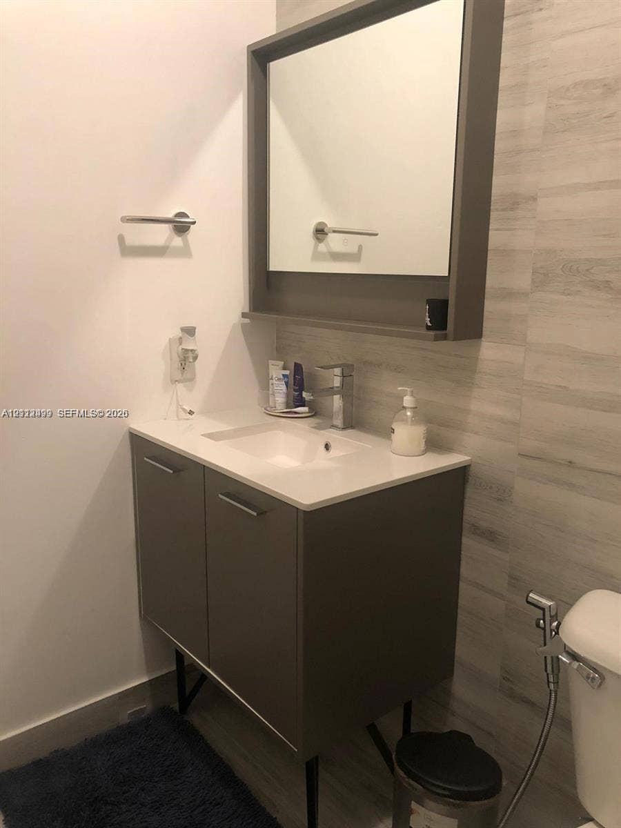 Vanity with a solid surface countertop, integrated sink, and metallic faucet, paired with a matching wall-mounted medicine cabinet and horizontal tile backsplash