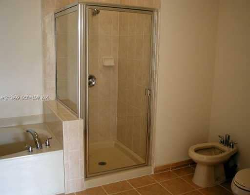 Corner shower enclosure with a chrome-framed glass door, tiled surround, and integrated soap dish, paired with a built-in soaking tub featuring a chrome faucet and a dedicated bidet