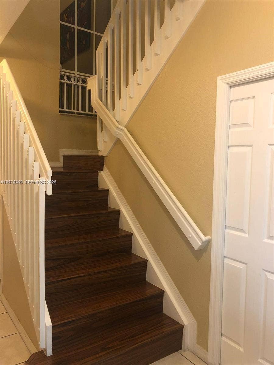 Staircase featuring wood-finish treads, white painted railings with balusters, and an integrated handrail