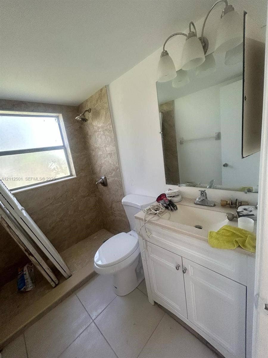 Bathroom featuring a white vanity cabinet with a solid surface countertop, an integrated sink with a chrome faucet, a three-light wall-mounted fixture, and a tile-surround shower