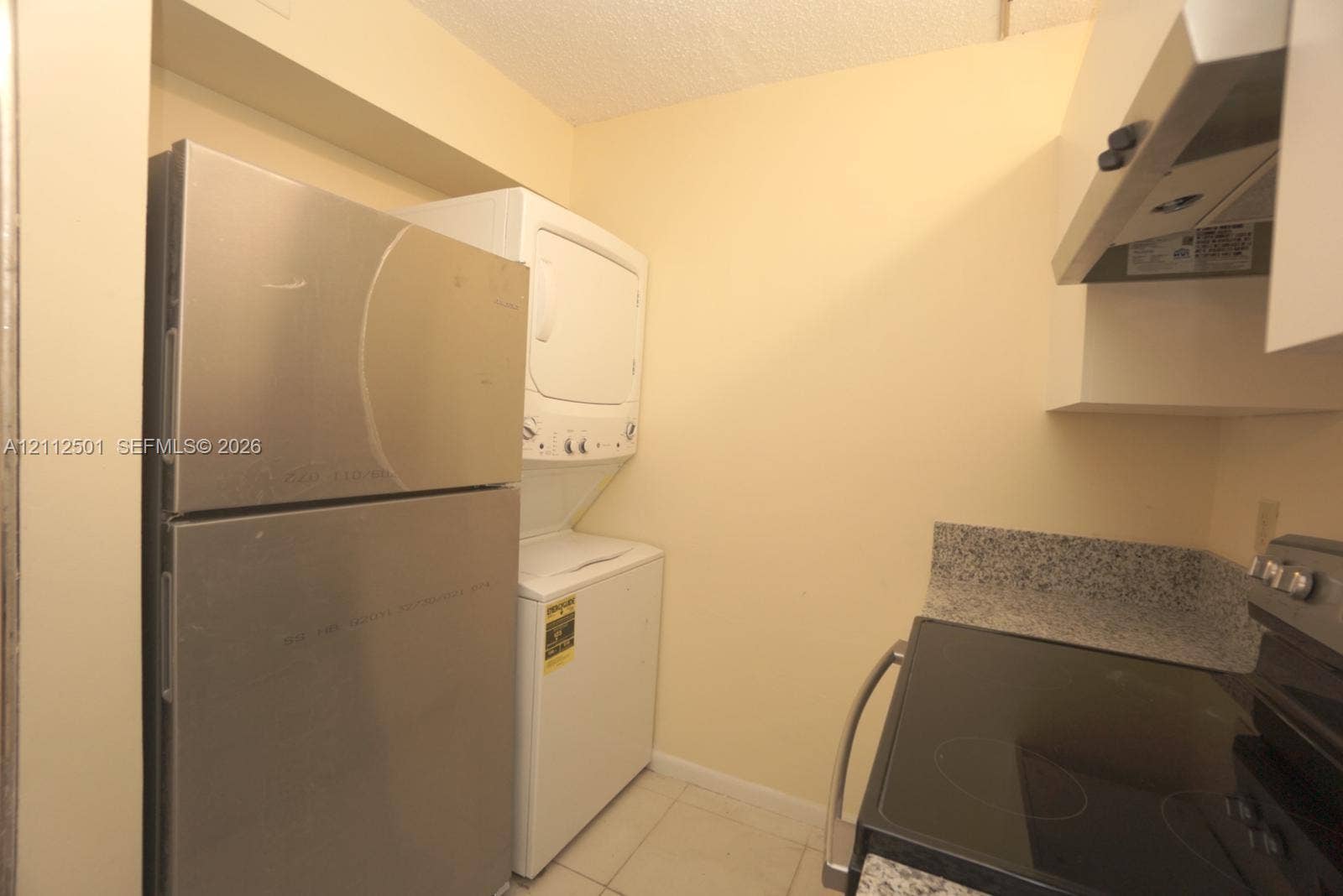 Stainless steel refrigerator, stackable laundry unit, stone-patterned countertops, electric range, and overhead cabinetry