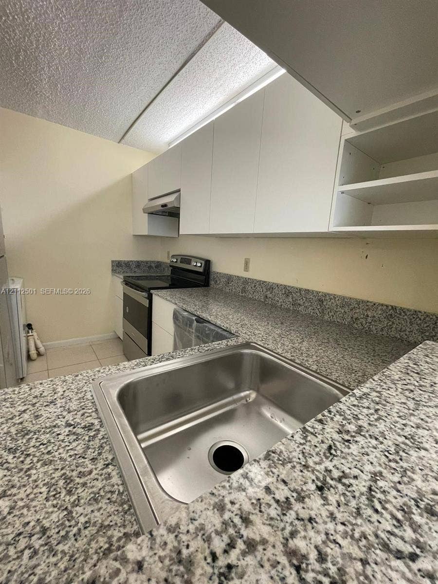 Kitchen featuring white flat-panel cabinetry, stone-finish countertops, stainless steel undermount sink, and stainless steel range