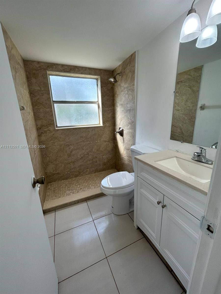 Bathroom featuring a white vanity with integrated basin, light-toned countertop, floor-to-ceiling textured tile shower surround, mosaic tile shower flooring, and large-format tile flooring