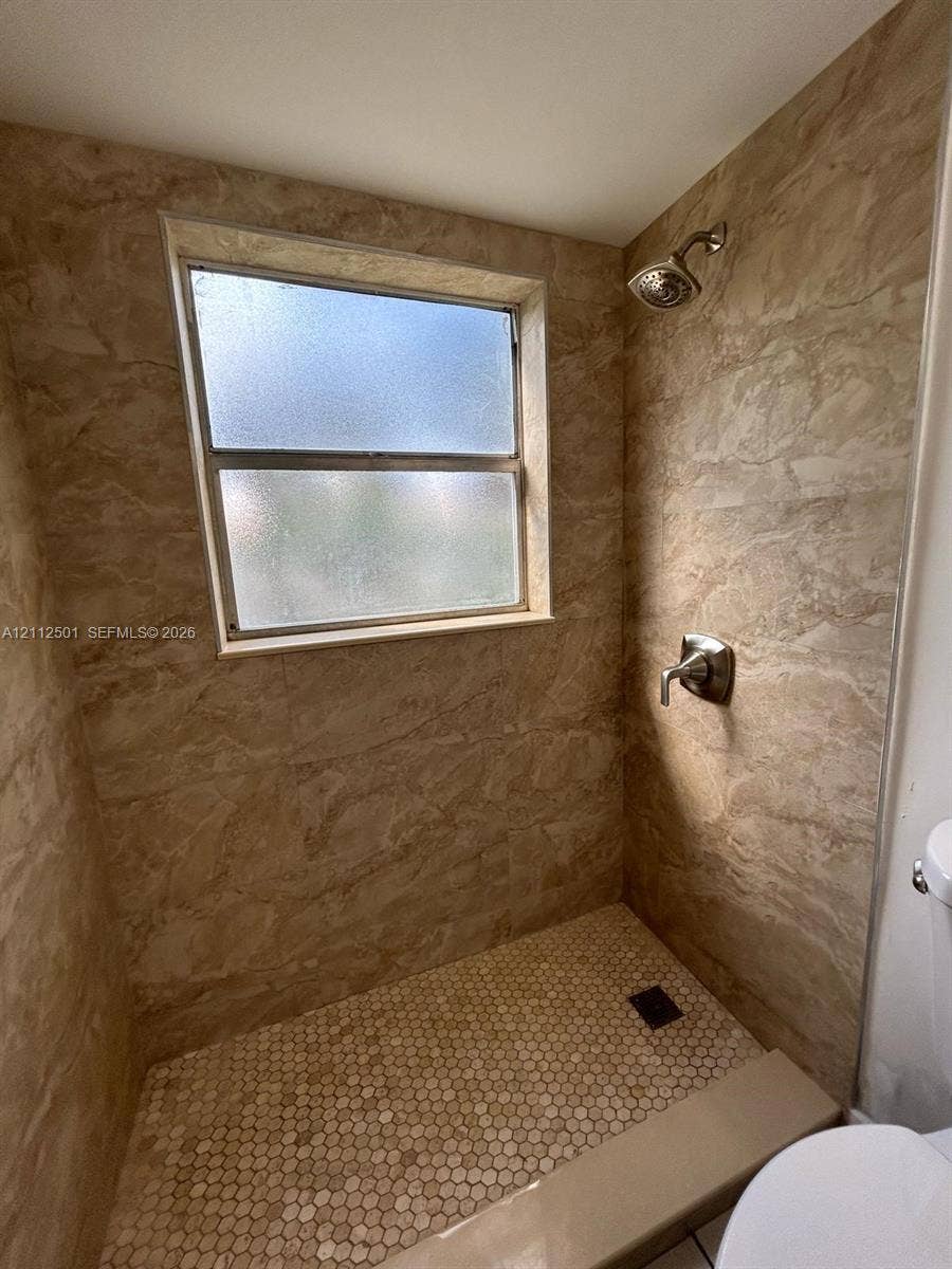 Walk-in shower featuring floor-to-ceiling large-format tile surround, hexagonal tile flooring, frosted glass window, and a single-handle polished metal shower fixture