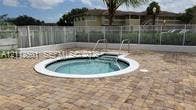 In-ground spa featuring a white border, metal handrails, and a surrounding paver patio enclosed by white fencing