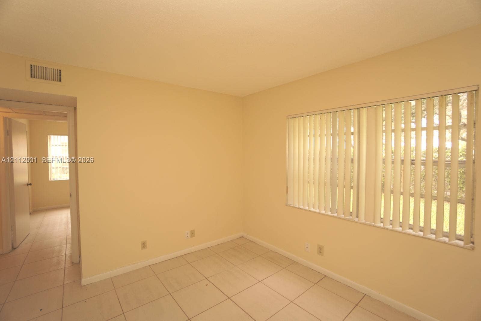 Interior space featuring light-toned tile flooring, neutral wall paint, and windows outfitted with vertical blinds